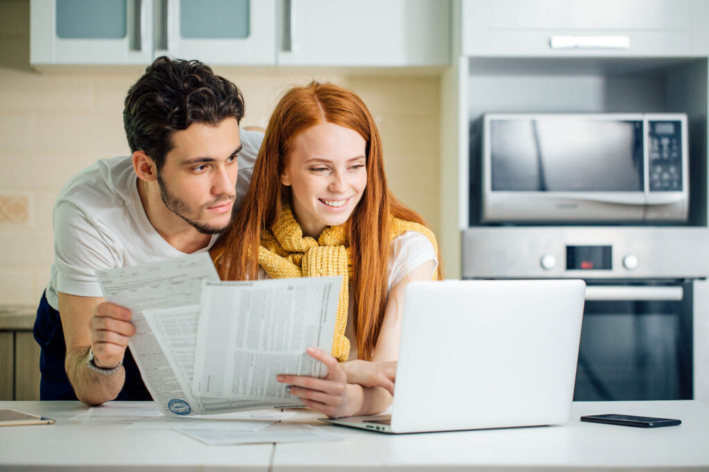 Happy couple at home paying bills with laptop and looking screen